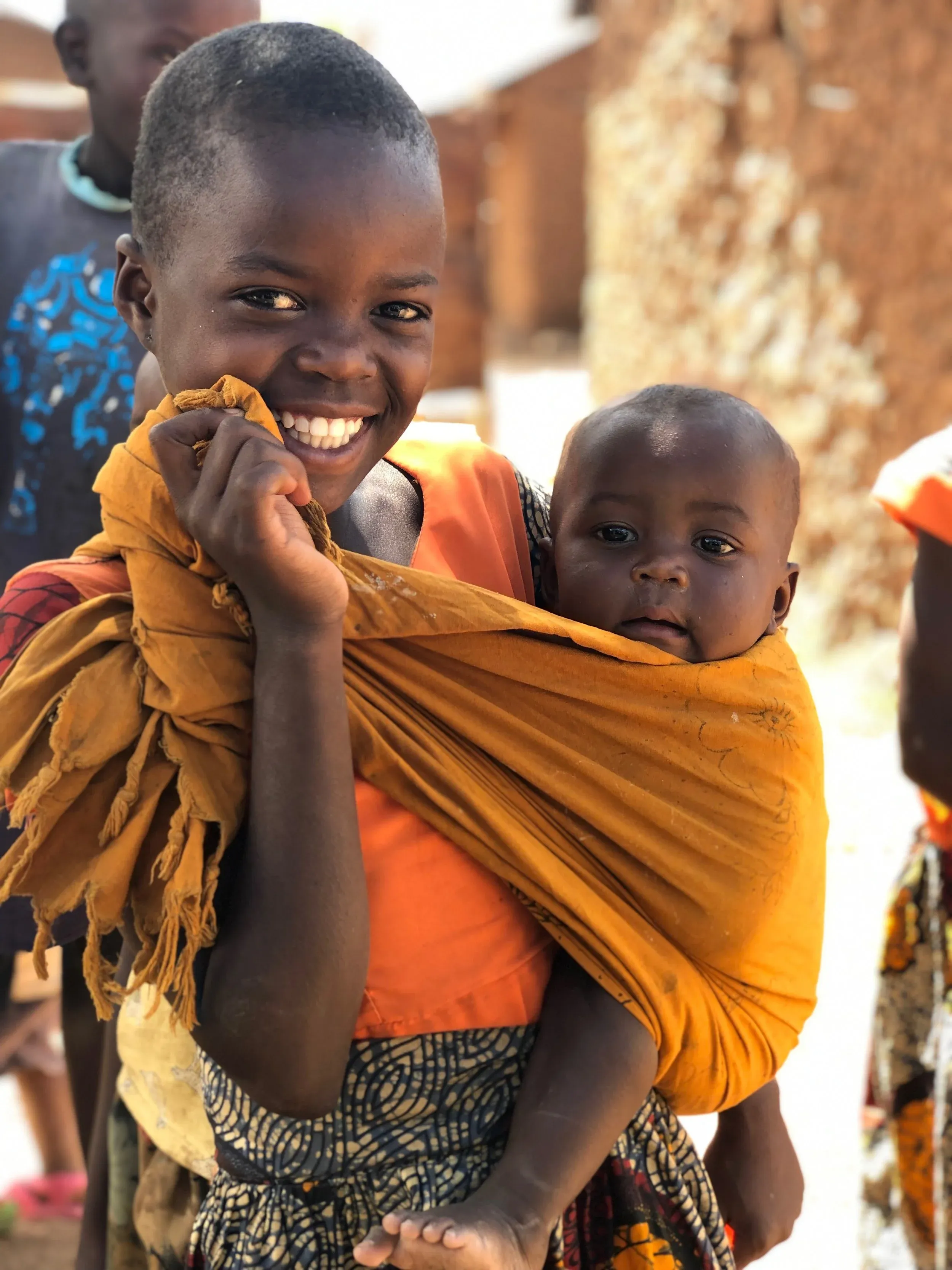 A young girl carrying her baby sibling in a traditional cloth wrap — a familiar scene of family life in rural Kenya